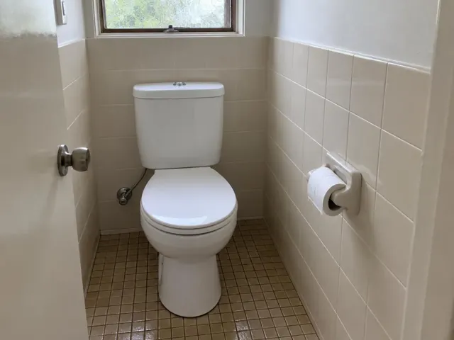Clean white toilet in a small tiled bathroom with window and toilet roll holder in Seven Hills