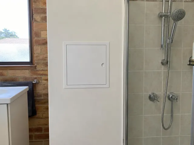 Small access panel in a painted bathroom wall beside a tiled shower in Quakers Hill